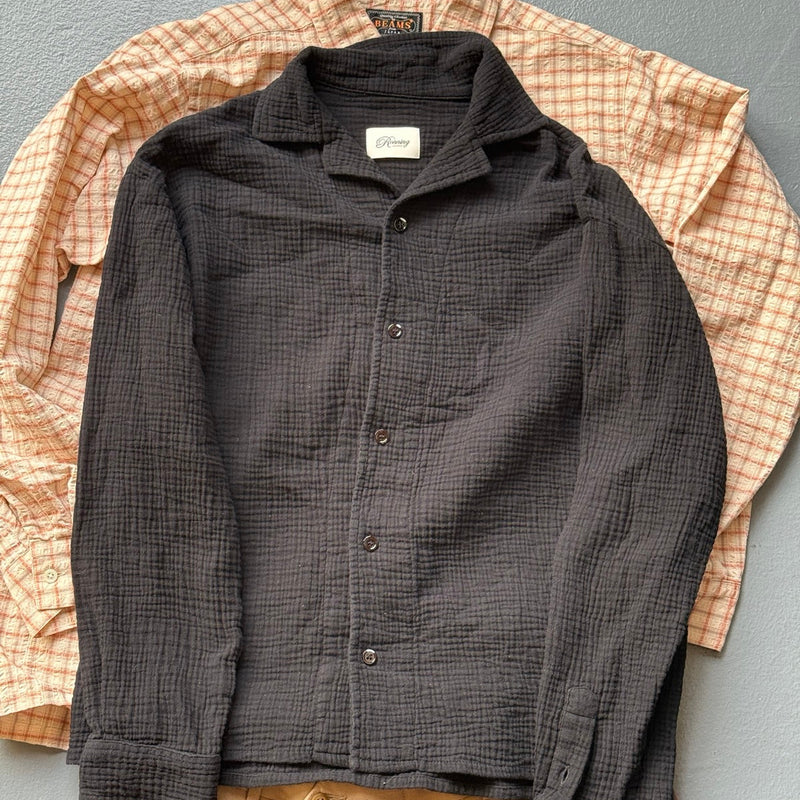 A black textured Ronning shirt laid over a BEAMS check shirt and pleated khaki trousers
